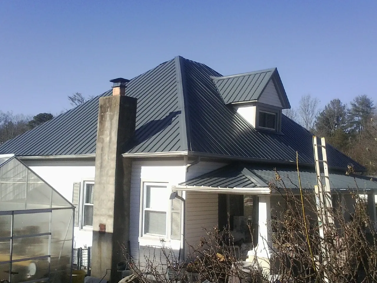 Dark blue standing seam metal roof on a white farmhouse with dormer — Slate & Tile Roof Repair by Roofing Brothers in South Jamesport