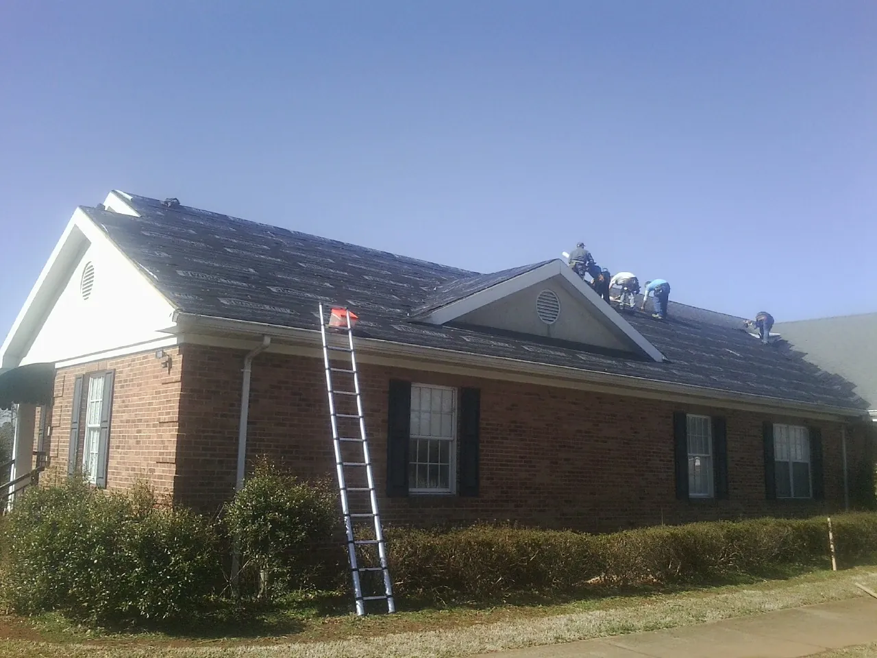 Crew tearing shingles off a brick ranch roof with a ladder set — Metal Roof Repair work by our crew in South Jamesport