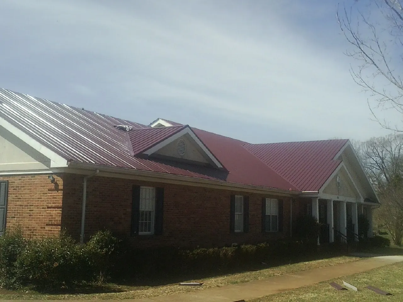 Red metal roof with gabled entries on a long brick building, from a Hail Damage Roof Repair job in South Jamesport