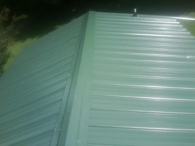 New green metal panels meeting at the ridge of a roof — Flat Roof Repair work by our crew in South Jamesport