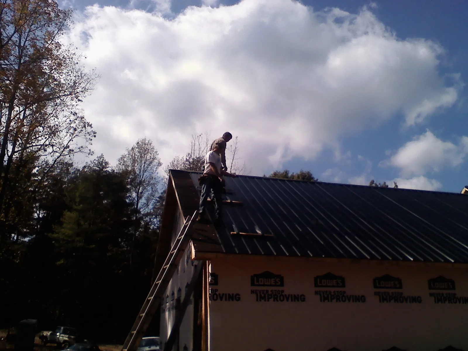 Roofer fastening dark metal panels high against a cloudy sky, from a Roof Inspection job in South Jamesport
