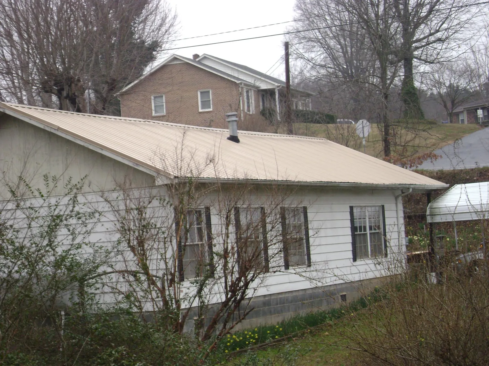 Tan metal roof on a white sided house set into a hillside — Commercial Roofing by Roofing Brothers in South Jamesport