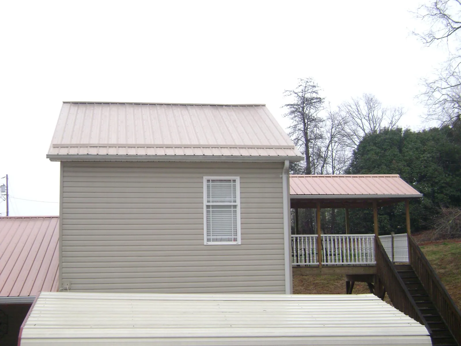 Tan metal roofs on a two story addition and attached porch, from a Roof Replacement job in South Jamesport